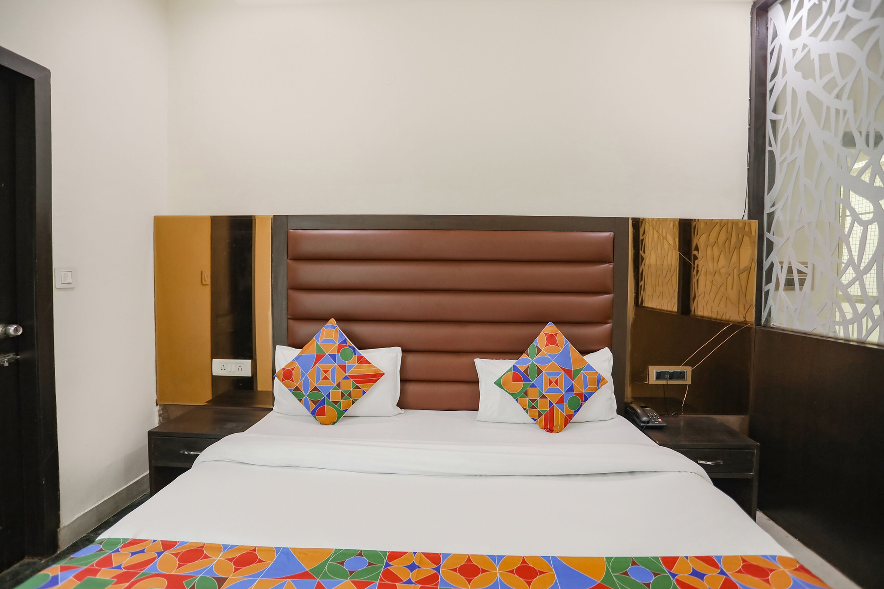 A hotel room with a large bed, two decorative pillows, a nightstand, and a wall-mounted phone.