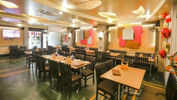 A restaurant with multiple tables and chairs, ceiling fans, and a television on the wall. - Fabexpress The Residency (Noida)
