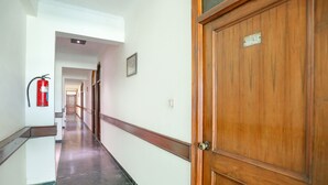 A hallway with a wooden door, a fire extinguisher, and a corridor leading to another room. - Fabexpress The Residency (Noida)
