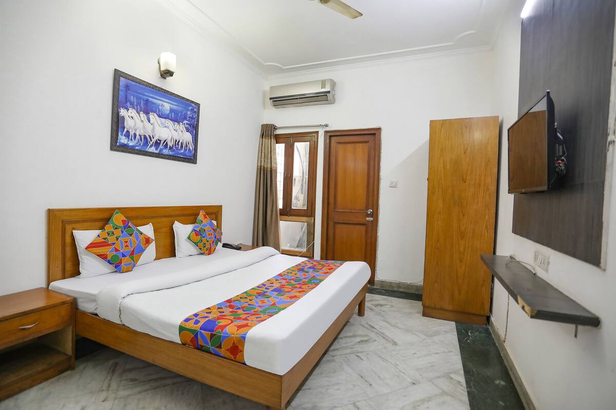 A hotel room with a wooden bed, a TV mounted on the wall, and a painting above the bed.