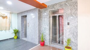 A modern lobby with marble walls, two elevators, and potted plants. - Fabhotel Prime Syn Grand (Hyderabad)