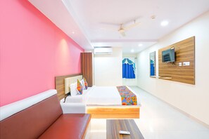 Quarto de hotel com cama, sofá, televisão na parede e ventoinha no teto.