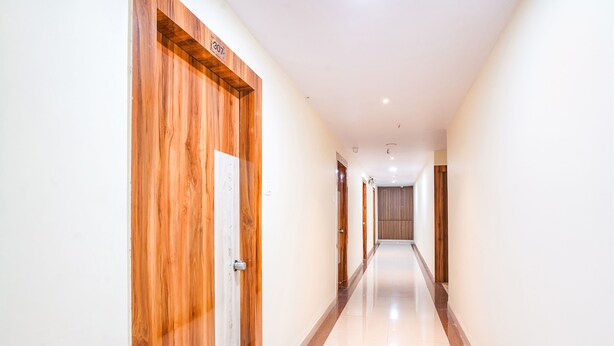 A long, narrow hallway with wooden doors on one side and a plain wall on the other. - Fabhotel Prime Syn Grand (Hyderabad)