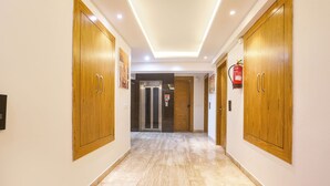 A hallway with wooden doors, a fire extinguisher, and a glass door at the end. - FabHotel Green Lotus Star 17 (New Delhi)