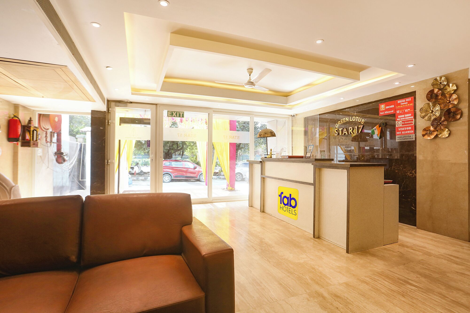 A hotel reception area with a leather couch, a reception desk, and a glass door leading outside.