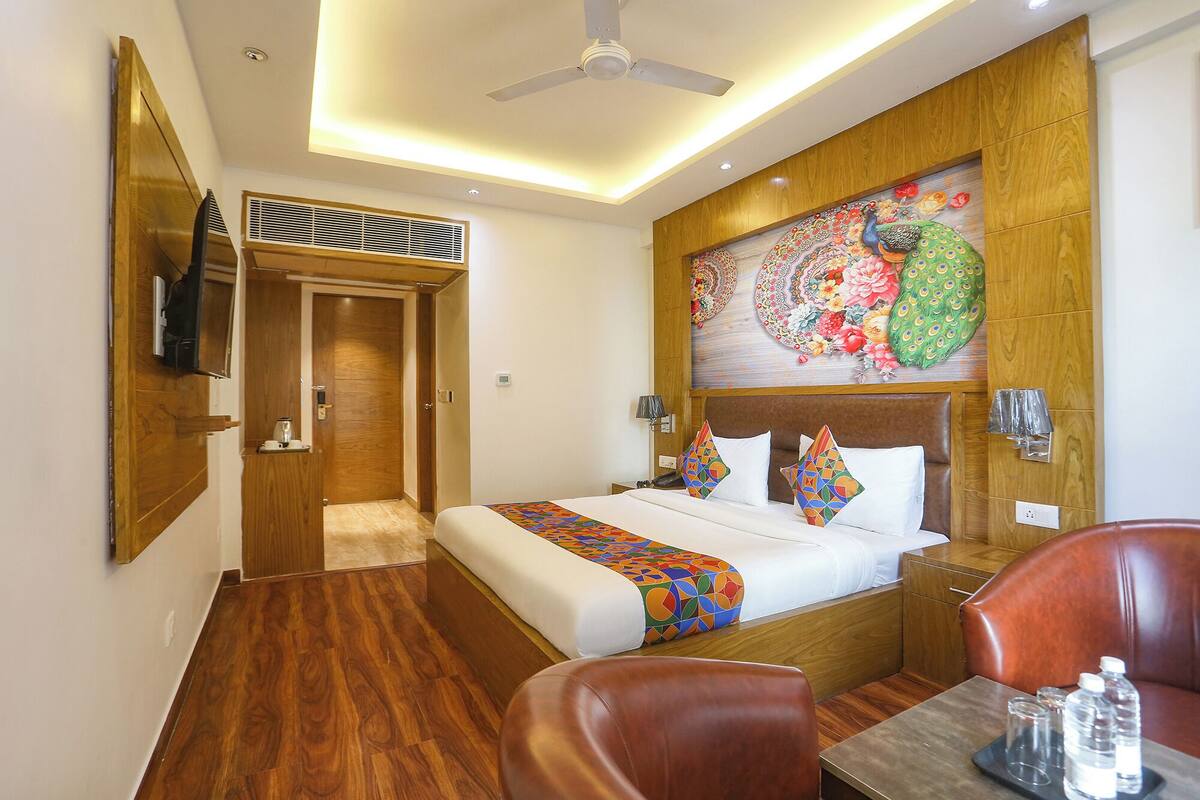 A hotel room with a bed, a desk, a chair, a ceiling fan, and a wall-mounted TV.