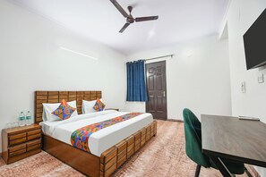 A bedroom with a wooden bed, a desk, a chair, a ceiling fan, and a door with curtains. - FabHotel Royal Casa (Gurugram)