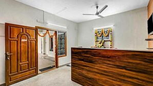 A reception area with a wooden reception desk, a ceiling fan, and a window with decorative garlands. - Fabexpress Aathira Inn (Chennai)