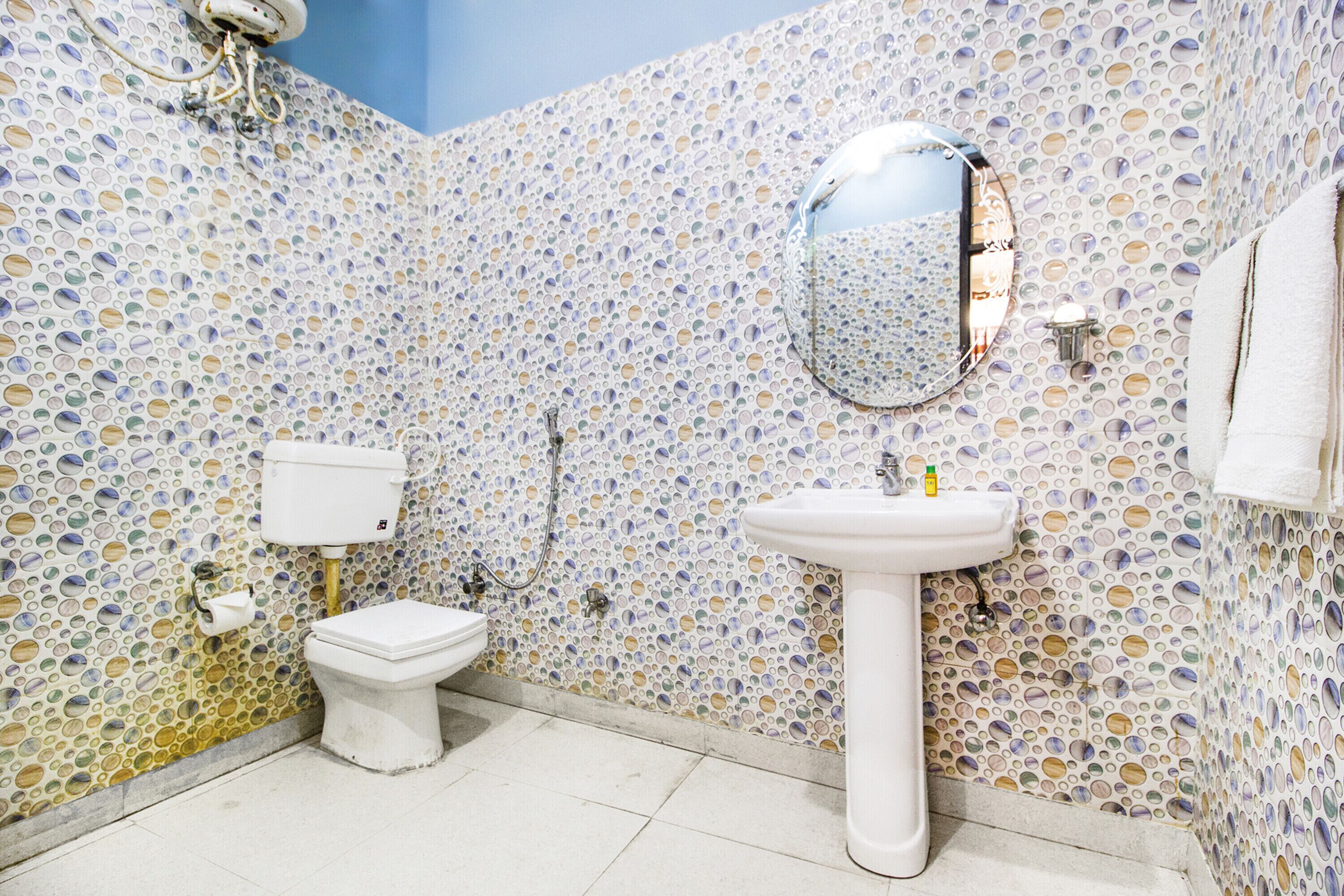 A bathroom with a mosaic tile wall, a toilet, a sink, and a mirror.