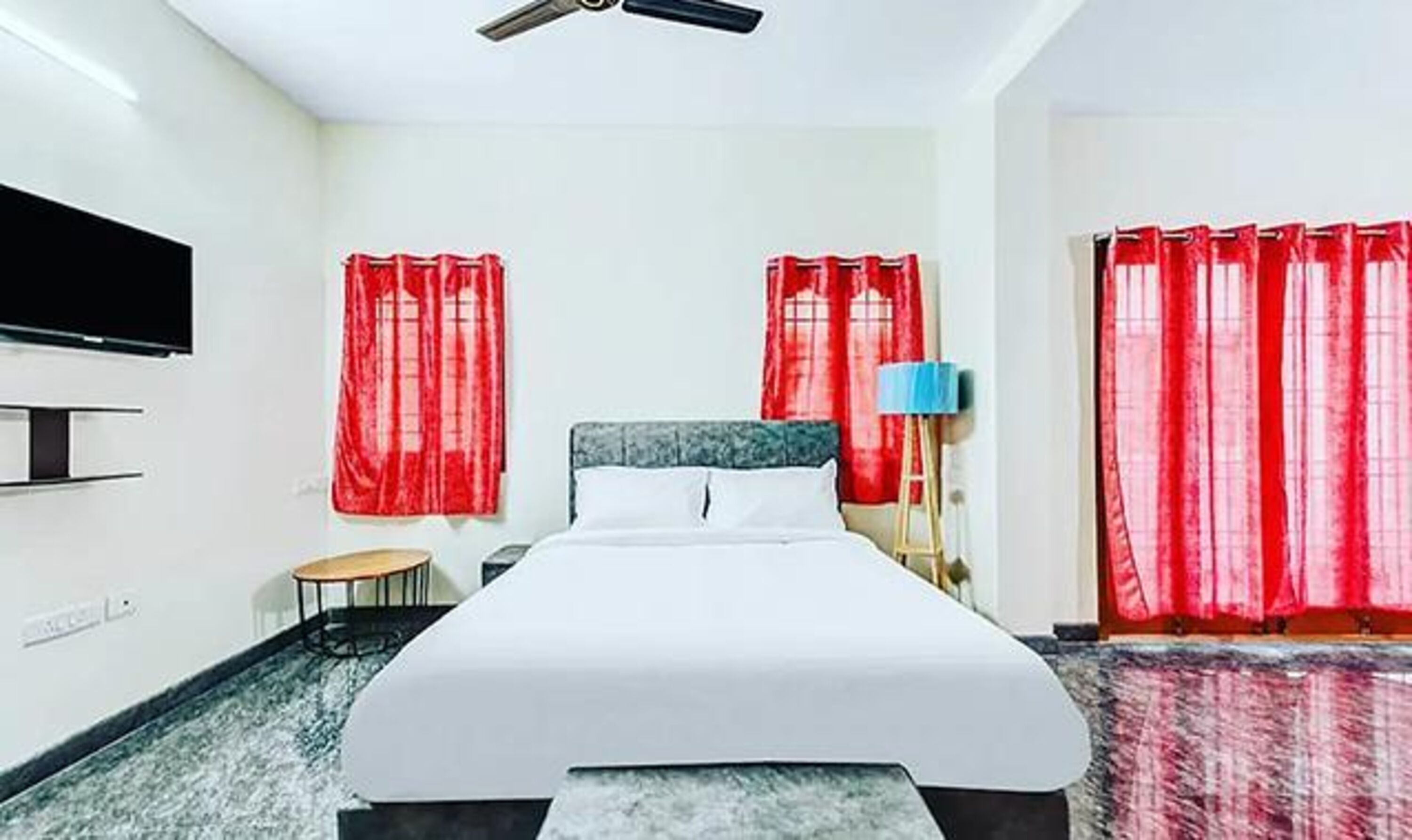 A hotel room with a bed, a TV, a lamp, and red curtains.