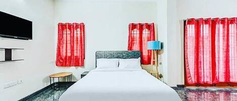 A hotel room with a bed, a TV, a lamp, and red curtains.
