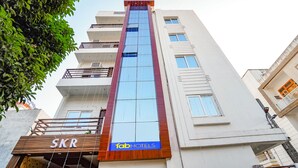 A modern hotel building with a prominent glass facade, a sign for 'SKR' and 'fabHOTELS' on the ground floor, and a tree to the left. - Fabhotel Sk Residency (Varanasi)