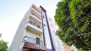 A multi-story hotel with a prominent 'SKR' sign at the entrance, balconies on each floor, and a large tree to the right. - Fabhotel Sk Residency (Varanasi)