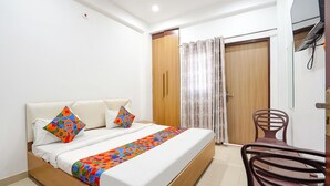 A bedroom with a bed, a chair, a wooden door, and a ceiling fan. - Fabhotel Sk Residency (Varanasi)