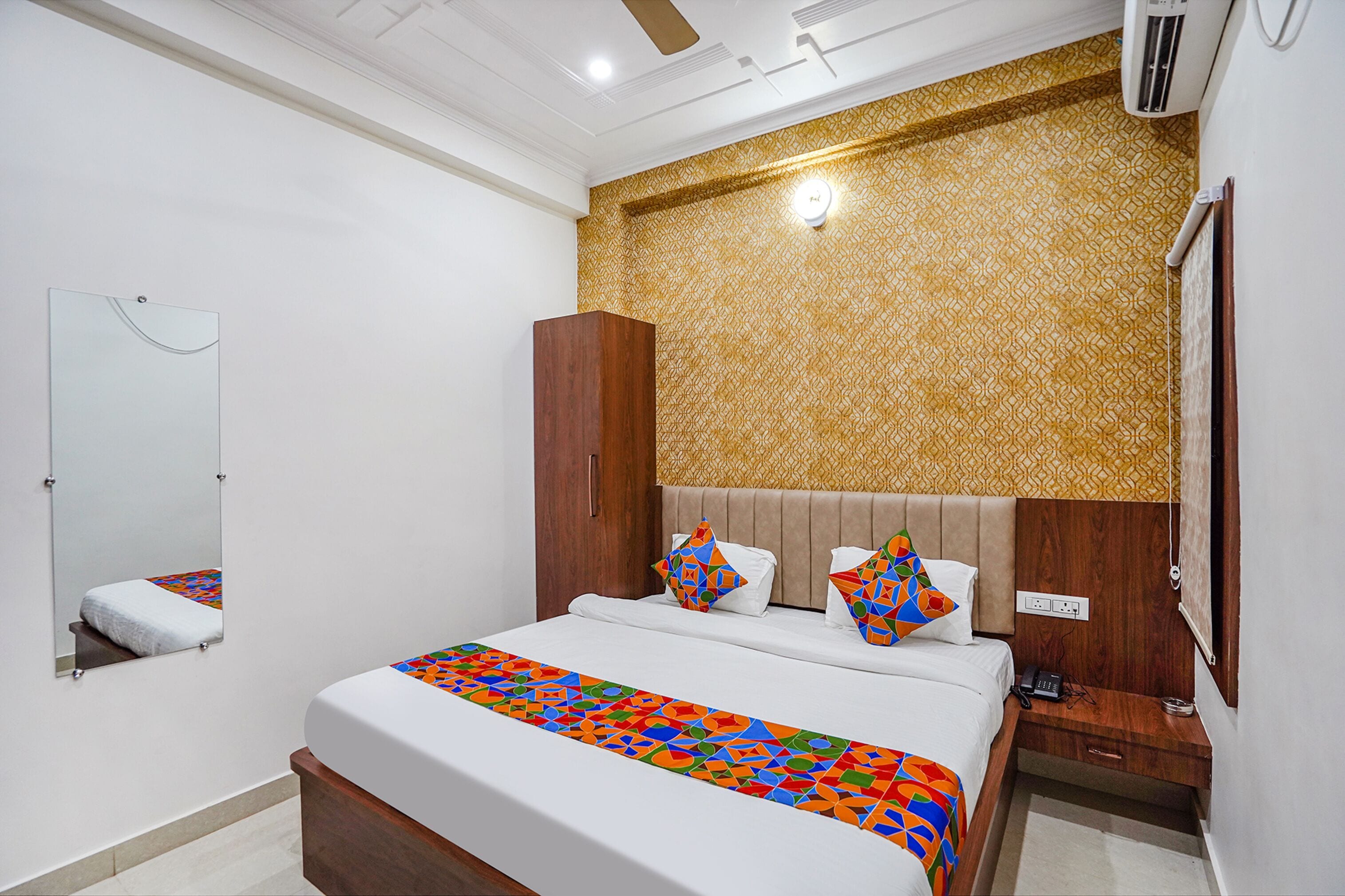 A hotel room with a bed, a bedside table, a mirror, and a wall with a patterned design.