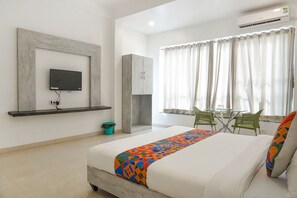 A hotel room with a bed, a TV mounted on the wall, a small table with chairs, and a window with curtains. - Fabhotel Irra Executive (Sasvad)