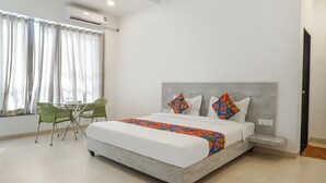 Una habitación de hotel con una cama grande, una mesita con sillas y un ventanal con cortinas.