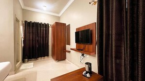 A hotel room with a wooden desk, a flat-screen TV mounted on the wall, a coffee maker, and a large window with curtains. - Fabhotel Gateway Suites (Bengaluru)
