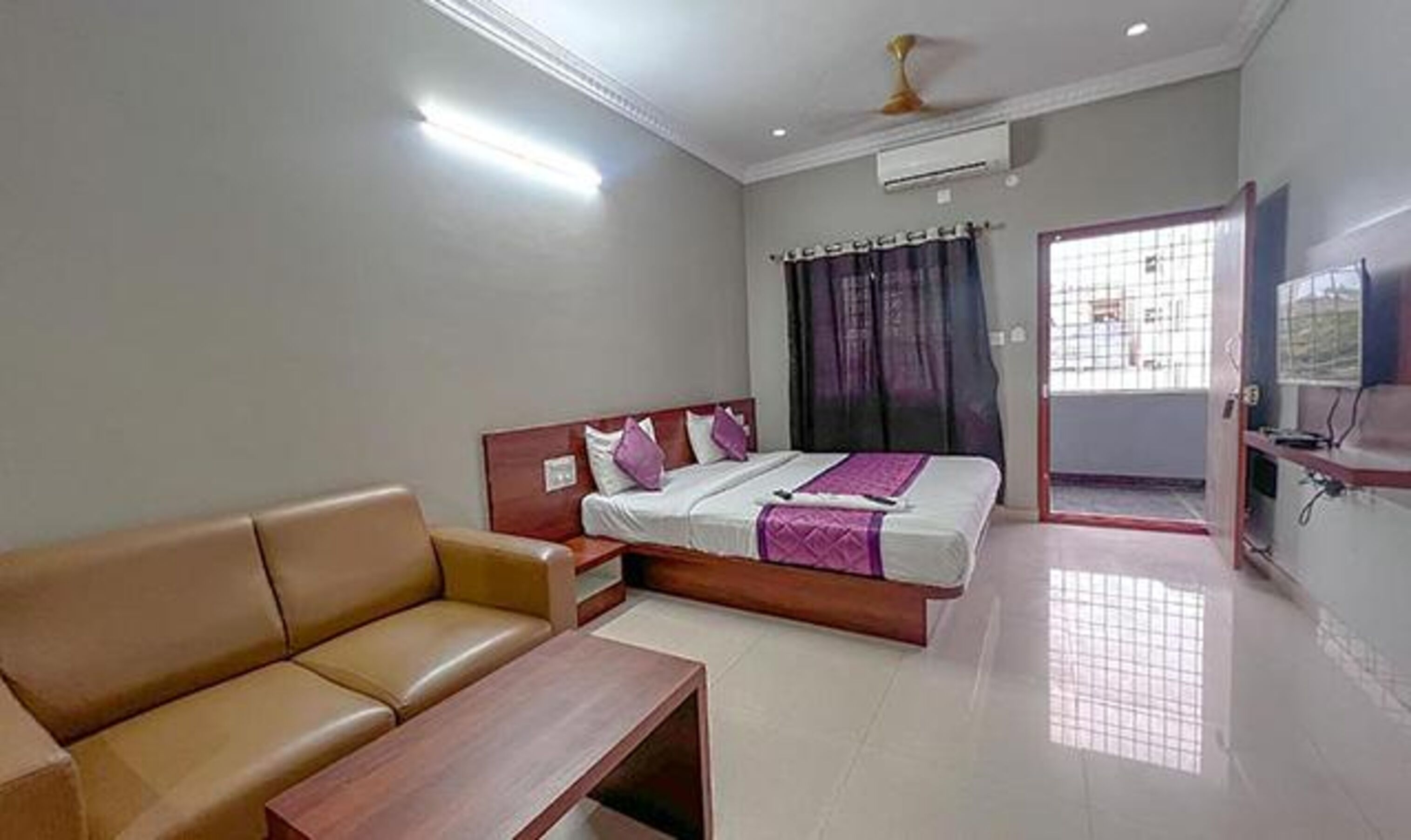 A hotel room with a bed, a sofa, a small table, and a TV.