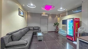 A modern lobby with a grey sectional sofa, a glass coffee table, a Coca-Cola refrigerator, and a door in the background. - Fabhotel Gateway Suites (Bengaluru)