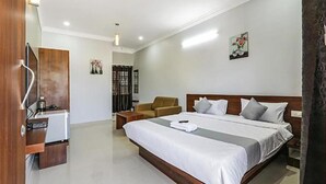 A hotel room with a large bed, a wooden headboard, a small seating area, and a kitchenette. - Fabhotel Gateway Suites (Bengaluru)