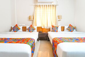 Habitació d'hotel amb dos llits, cadascun amb llençols de colors i patrons geomètrics, una nitzeta de fusta, una taula petita i un aire condicionat fixat a la paret.