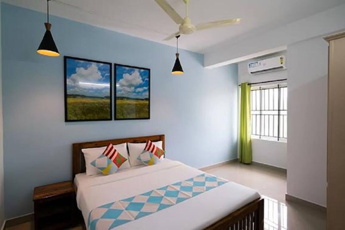 A bedroom with a bed, two wall-mounted lights, a ceiling fan, a window with bars, and two landscape paintings.
