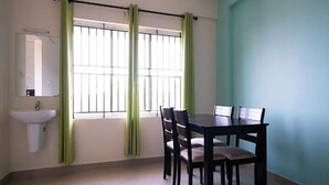 Une pièce comprenant une table et des chaises, une fenêtre avec des rideaux verts et un évier blanc.