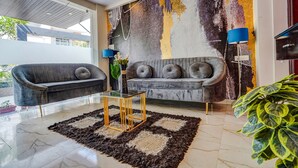 A modern living room with two grey sofas, a glass coffee table, and a large abstract mural on the wall. - Fabhotel Olive Stay Inn (Nagpur)