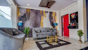 A modern living room with a grey sofa, a grey armchair, a small table with a vase, and a decorative wall with a red door in the background. - Fabhotel Olive Stay Inn (Nagpur)
