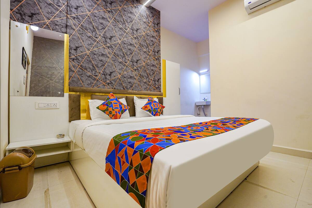 A modern hotel room with a large bed, a marble-patterned wall, and a bathroom visible in the background.