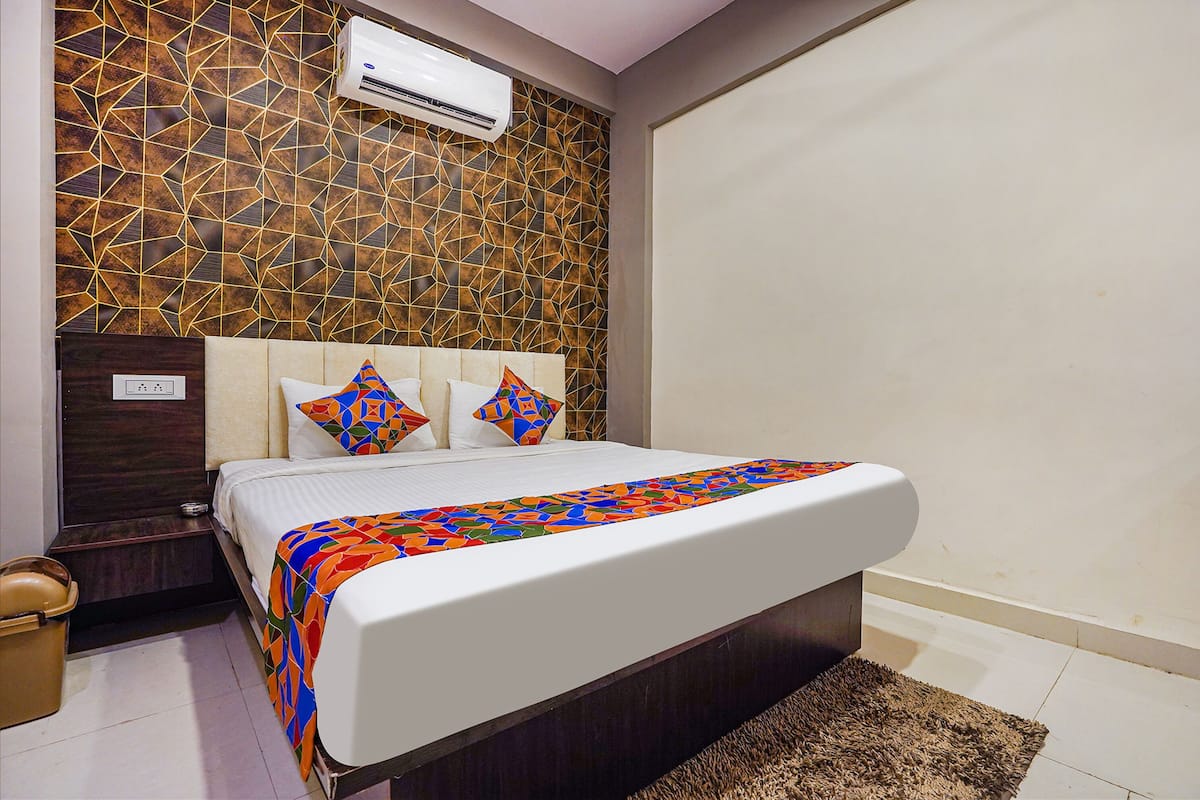 A hotel room with a patterned wall, a bed with a colorful bedspread, and a brown rug.
