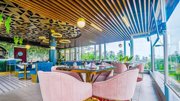 Een modern restaurant met een geometrisch plafond, grote ramen en roze stoelen.