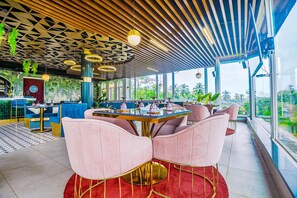 En moderne restaurant med et geometrisk loft, store vinduer og lyserøde stole.