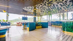 Een modern restaurant met een geometrisch plafondontwerp, blauwe en gele zitplaatsen en uitzicht op de heuvels.