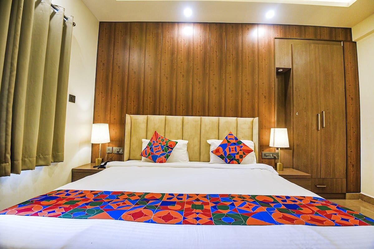 A hotel room with a large bed, wooden headboard, two nightstands with lamps, a wardrobe, and a colorful bedspread.