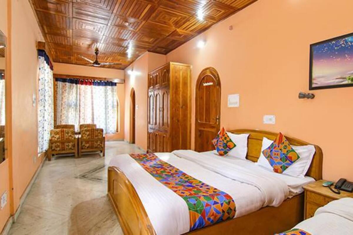 A hotel room with a wooden ceiling, a bed with colorful bedding, a desk with a phone, and a painting on the wall.