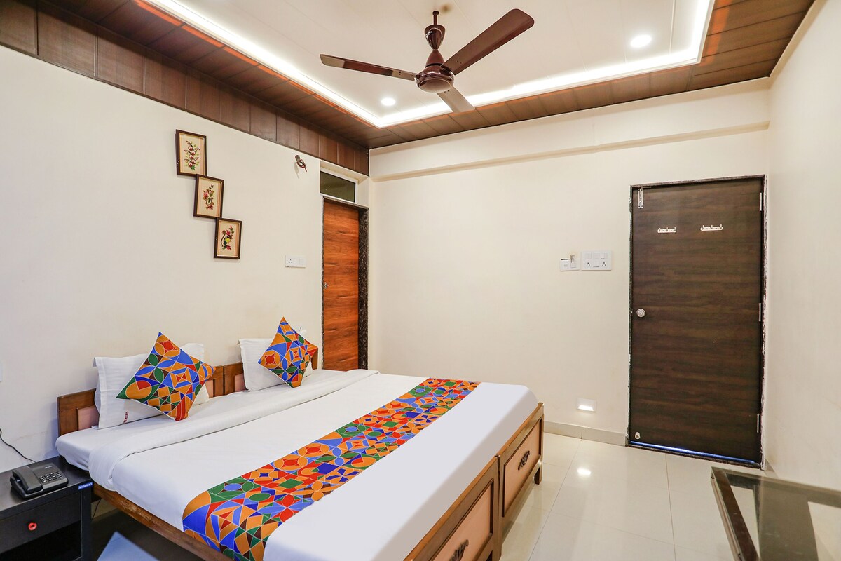 A bedroom with a bed, wooden headboard, a ceiling fan, a door, and a small table with a phone.