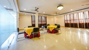 A conference room with tables and chairs, large windows with curtains, ceiling fans, and a chandelier. - Fabexpress Alaknanda Paradise (Dehradun)
