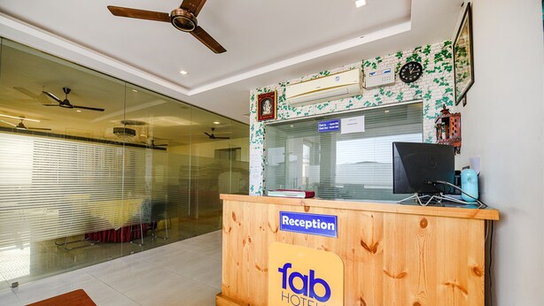 A reception desk at a hotel with a wooden finish, a ceiling fan, and a clock on the wall. - Fabexpress Alaknanda Paradise (Dehradun)