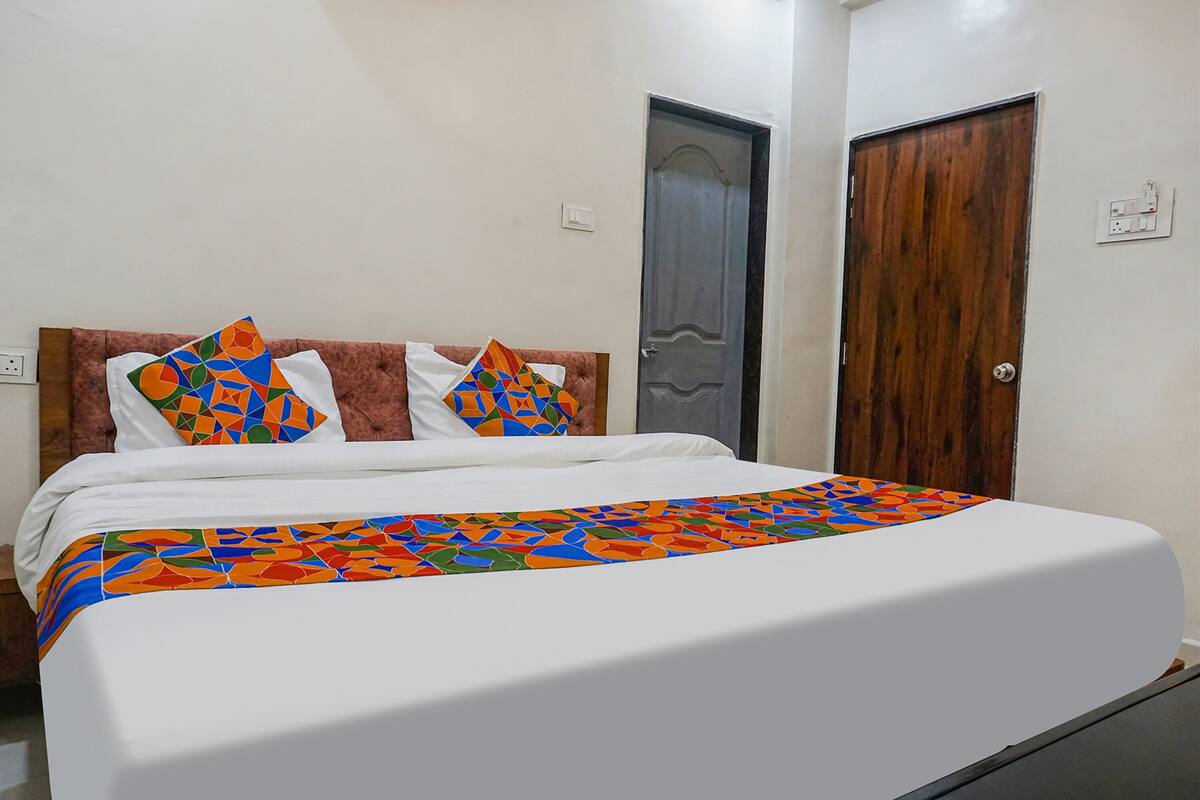 A bed with a colorful geometric-patterned bedspread and two pillows, a wooden headboard, and two doors, one of which is partially open.
