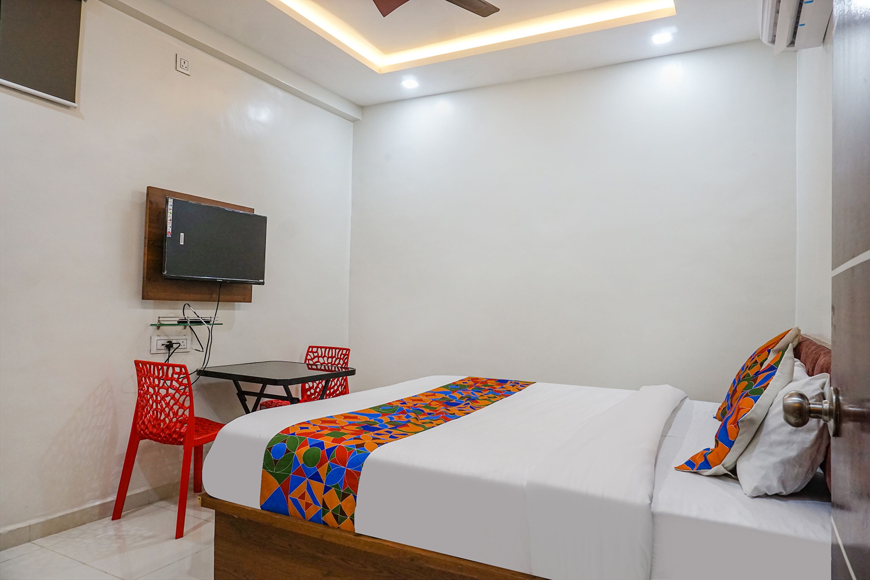 A hotel room with a bed, a TV mounted on the wall, a small table, and a red chair.