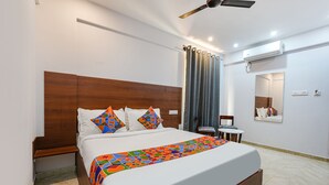 A neatly arranged bedroom with a bed, a chair, a small table, and a mirror. - Fabhotel Tree Suites (Bengaluru)