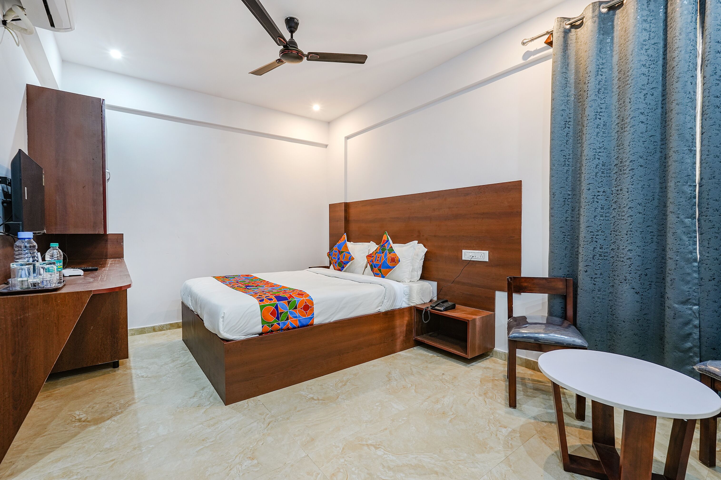 Habitación de hotel con cama de madera, un escritorio con silla, una mesita y un ventilador de techo.