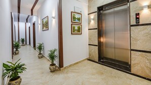 A hotel lobby with a marble floor, wooden beams, potted plants, framed pictures, and an elevator. - Fabhotel Tree Suites (Bengaluru)