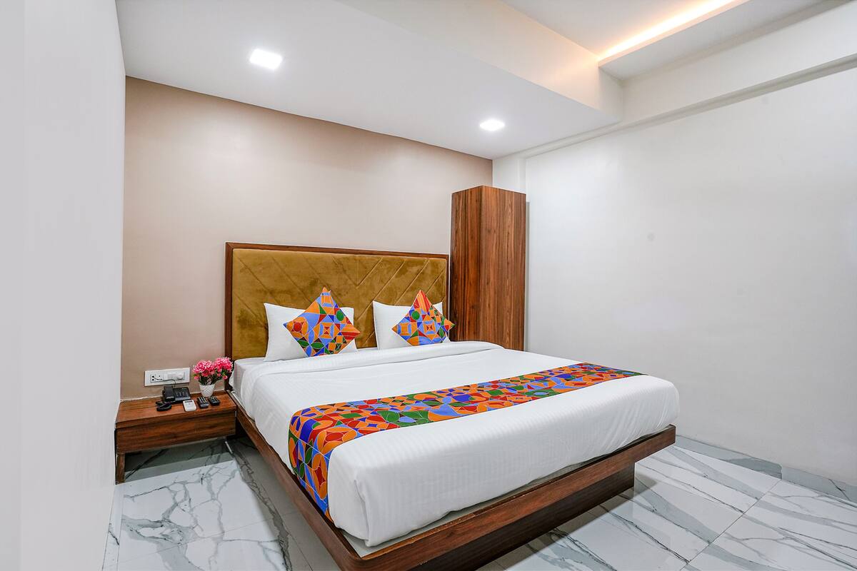 A neatly arranged hotel room with a large bed, a wooden nightstand, a bedside table, and a wardrobe.