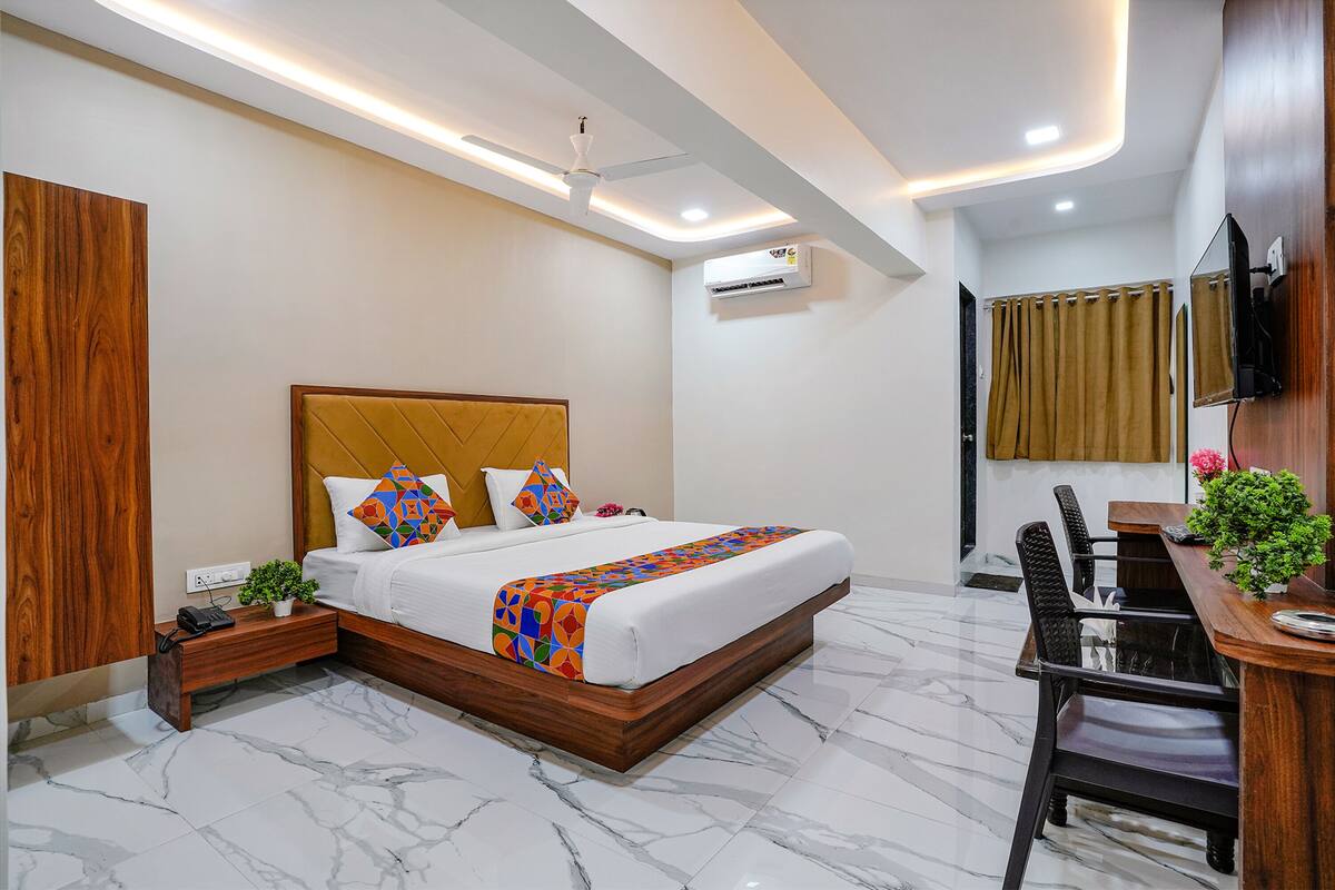 A modern hotel room with a large bed, a desk with a chair, a TV mounted on the wall, and an air conditioning unit.