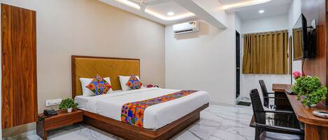 Una habitación de hotel moderna con una cama grande, un escritorio con silla, un televisor montado en la pared y un equipo de aire acondicionado.