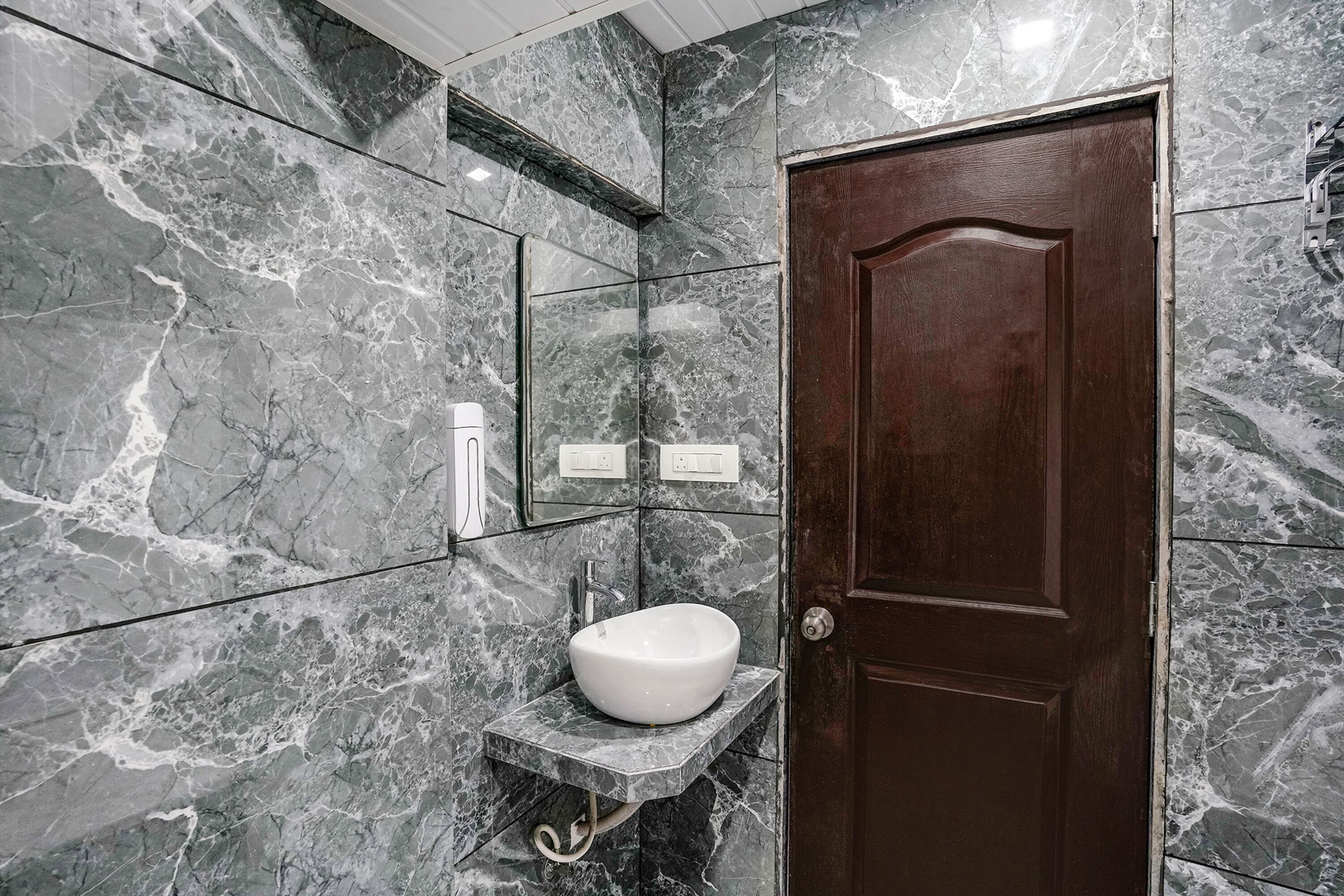 Un bagno con una parete in marmo, una porta in legno e un lavandino bianco.