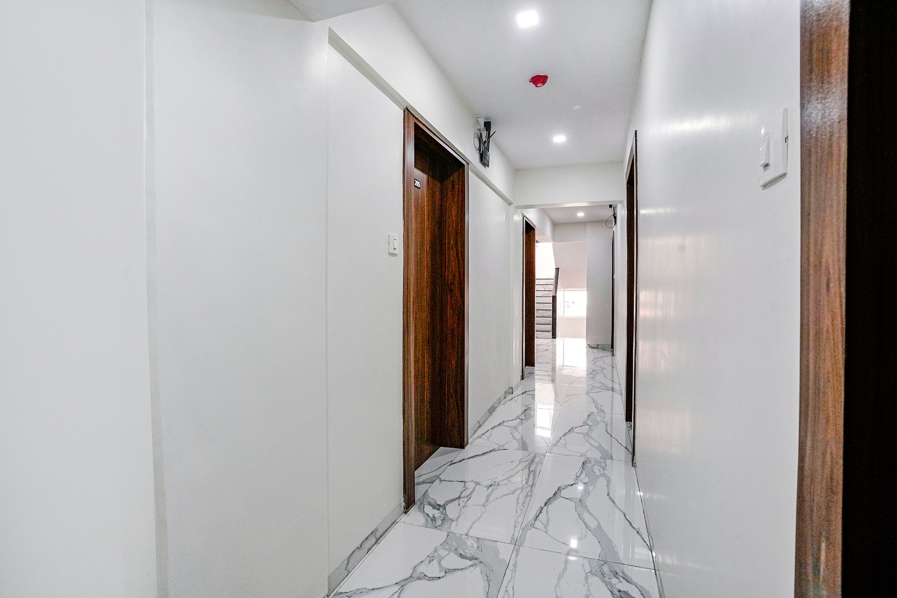 A hallway with white walls and a marble floor, leading to a staircase.